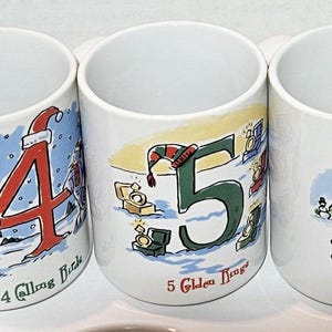 May include: Set of six white ceramic mugs with illustrations of numbers 2 through 8 and corresponding Christmas-themed phrases. Each mug features a different illustration and phrase, such as "2 Turtle Doves" and "8 Maids a-Milking".