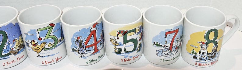 May include: Set of six white ceramic mugs with illustrations of numbers 2 through 8 and corresponding Christmas-themed phrases. Each mug features a different illustration and phrase, such as "2 Turtle Doves" and "8 Maids a-Milking".