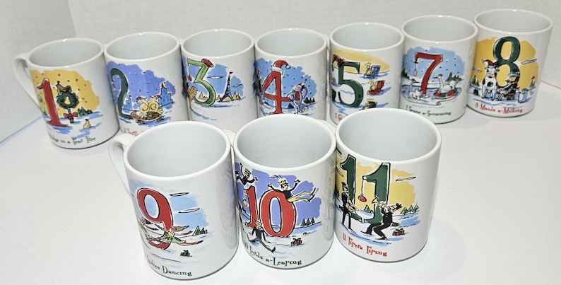 May include: Set of 12 white ceramic mugs with colorful illustrations and numbers 1 through 12. Each mug features a different Christmas-themed scene with a corresponding number.