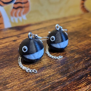 Może przedstawiać: Para czarno-białych kolczyków. Każdy kolczyk to czarna kula z białymi, uśmiechniętymi ustami i srebrnym łańcuszkiem. Kolczyki mają srebrne haczyki do przekłutych uszu.
