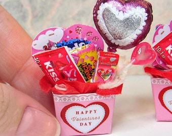 May include: A pink and red Valentine's Day gift basket filled with candy, a heart-shaped balloon, and a lollipop. The basket is decorated with a white lace trim and a heart-shaped label that says "Happy Valentine's Day".