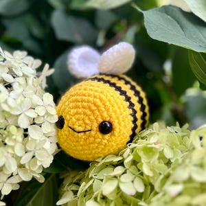 K&ouml;nnte beinhalten: Ein geh&auml;keltes Bienentier mit schwarzen und gelben Streifen, wei&szlig;en Fl&uuml;geln und schwarzen Augen. Die Biene sitzt auf einem Bett aus wei&szlig;en Blumen.