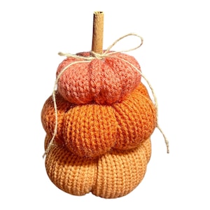 Könnte beinhalten: Gestapelte, gestrickte Kürbisdekoration in Orange- und Pfirsichtönen. Der Kürbis hat einen Zimtstiel und ist mit Bindfaden gebunden. Die handgefertigte Herbstdekoration ist perfekt für den Herbst.