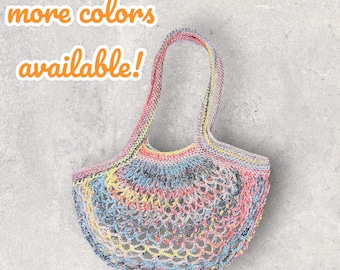 Può includere: Una borsa a rete di uncinetto colorata con un manico. La borsa è realizzata in diversi colori, tra cui rosa, blu, giallo e verde. Il testo "più colori disponibili!" è scritto in arancione sopra la borsa.