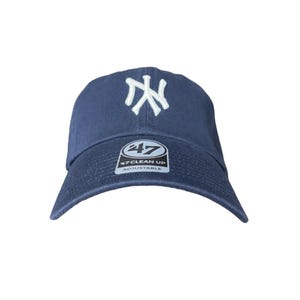 May include: Navy blue baseball cap with a white embroidered NY logo on the front. The cap has a curved brim and an adjustable strap. The tag reads "47 Clean Up Adjustable".