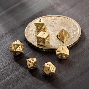 Könnte beinhalten: Ein Satz von sechs goldenen Metallwürfeln mit verschiedenen Zahlen auf jeder Seite. Die Würfel sind auf einer Silberdollar-Münze angeordnet.