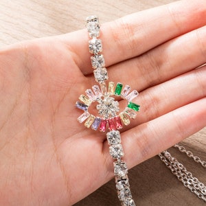 May include: A silver chain bracelet with a colorful eye charm. The eye is made of clear and colored rhinestones. The chain is made of small, clear rhinestones.