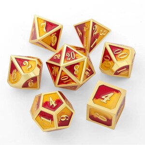 May include: Set of seven polyhedral dice in gold and red. Each die features a gold base with red accents and white numbers. The dice are designed for tabletop role-playing games and are arranged on a white surface.