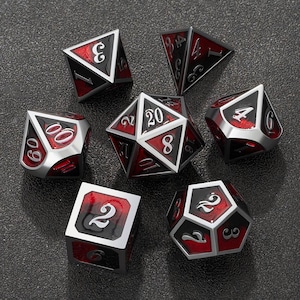 Puede incluir: Un conjunto de siete dados poliédricos para juegos de mesa. Los dados son plateados con detalles en negro y rojo. Cada dado tiene números blancos. Los dados están dispuestos sobre una superficie gris oscuro.