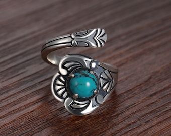 Peut inclure: Une bague en argent avec une pierre turquoise sertie dans un motif décoratif. La bague est ouverte et s'enroule autour du doigt.