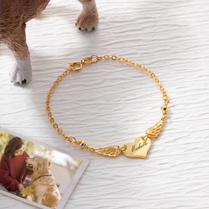 May include: Gold chain bracelet with a heart charm engraved with the name "Michelle" and angel wings.