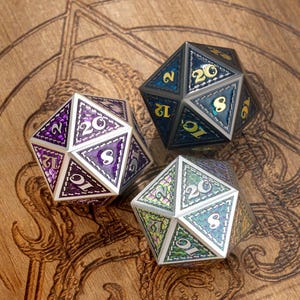 May include: Three iridescent metal dice with a 20-sided design. Each die has a different color scheme: purple, blue, and green. The dice are on a wooden surface.