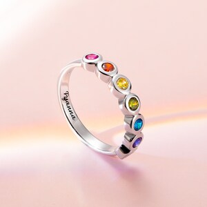Può includere: Un anello d'argento con un arcobaleno di pietre preziose colorate. L'anello è inciso con il nome "Byanna".