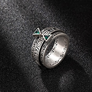 May include: A silver ring with a rotating band featuring numbers and a green triangular design. The ring has a detailed, intricate design.