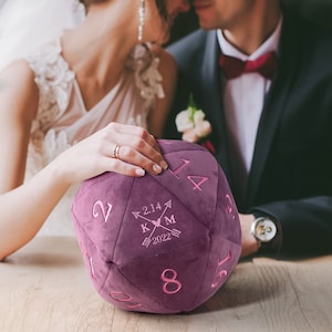 May include: A purple plush dice with pink embroidered numbers and a personalized message that reads "K+M 2.14.2022" with arrows and a heart.