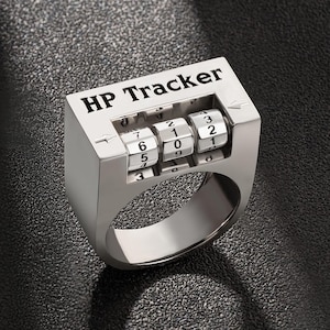 May include: A silver ring with a combination lock design. The ring has the words "HP Tracker" engraved on the top. The lock has four dials with numbers 0-9.