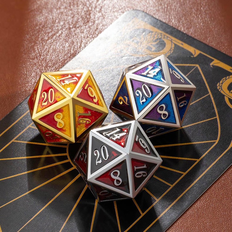 May include: Three multi-sided dice for tabletop games. One die is gold with red and yellow accents, another is silver with red and black, and the third is silver with blue and purple. Each die has white numbers.