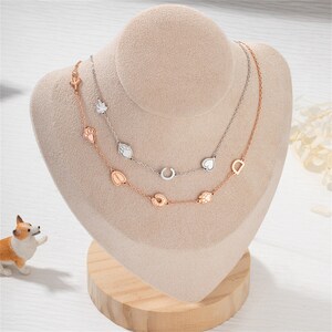Puede incluir: Dos delicados collares de oro con dijes. El collar superior tiene un dije de herradura, corazón y lágrima. El collar inferior tiene un dije de herradura, huella de pata y corazón.