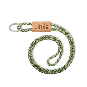 Puede incluir: Un cordón verde y marrón con estampado y una etiqueta de nombre de madera que dice "Linda".
