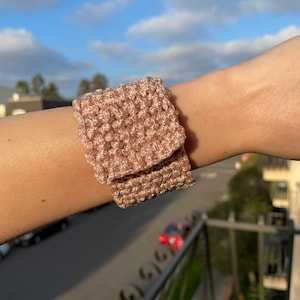 May include: A pink crocheted watch band with a folded design.