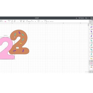 May include: Two pink and brown numbers, 22, shaped like donuts with sprinkles. The number 2 on the left is pink and the number 2 on the right is brown with purple, yellow, and teal sprinkles.