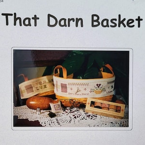 May include: A printed paper with the title "That Darn Basket" and an image of a cross-stitch basket with other cross-stitch items. The paper also includes the text "HILLSIDE SAMPLINGS" and contact information.