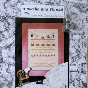 May include: A packaged cross-stitch kit titled "a needle and thread" with a framed design featuring text and stitched images of bells, pumpkins, and other objects. The kit includes small metal charms and is from ThreadBear Creations.