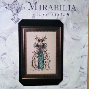 May include: A Mirabilia cross-stitch pattern kit featuring a framed design with a teal and gold figure, surrounded by floral and leaf accents. The kit is set against a white background with a rose pattern and includes the text "Mirabilia cross-stitch".