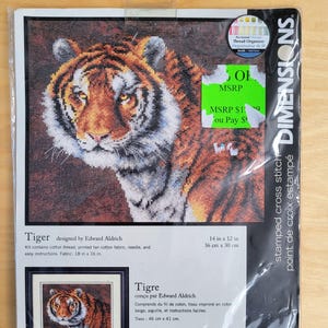 May include: A Dimensions stamped cross stitch kit featuring a detailed tiger design by Edward Aldrich. The kit includes cotton thread, a printed tan cotton fabric, a needle, and instructions. Fabric size is 18 in x 16 in.