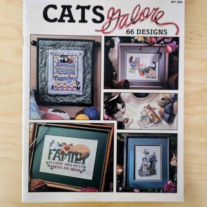 May include: A book cover with the title "Cats Galore" and a subtitle "66 Designs". The cover features several images of cross-stitch patterns featuring cats. The book is from Leisure Arts.