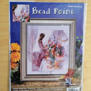 May include: A bead point kit with a framed picture of a woman arranging flowers. The kit includes pre-sorted glass beads, a needle, and thread. The picture measures 8 x 10 inches (20 x 25 cm). The kit is packaged in a clear plastic bag.