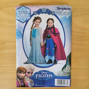 May include: A Simplicity home sewing pattern envelope, number 1233, for Disney Frozen costumes in US sizes 3-8. The package features illustrations of two children wearing blue and pink dresses with capes, alongside images of the characters Anna and Elsa.