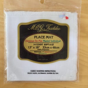 May include: A white place mat in a clear plastic package. The label reads "M.C.G. Textiles PLACE MAT" and lists dimensions as 13" x 18" (33cm x 46cm). The label also includes fabric washing instructions.
