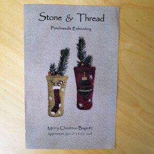 May include: A printed fabric featuring two Christmas-themed punchneedle embroidery designs. The designs include a stocking and an ornament, each with evergreen sprigs. The text reads "Stone & Thread" and "Merry Christmas Bags #2". Approximate size: 2" x 4-1/2" each.