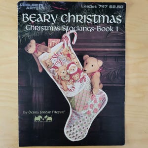 May include: A book cover titled "Beary Christmas Christmas Stockings-Book 1" features a Christmas stocking design with teddy bears. The cover has a dark background with a Christmas tree branch design. The author's name is Debra Jordan Meyer.