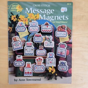 May include: A cross-stitch pattern book titled "Message Magnets on Vinyl-Weave" by Ann Townsend. The cover features various cross-stitched magnets with phrases like "Follow your heart" and "I love chocolate." The color palette includes blues, reds, and greens.