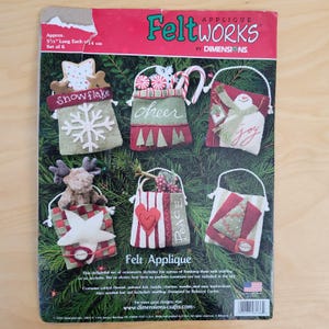 May include: Feltworks Christmas ornament kit with six felt applique designs. Each ornament is approximately 5.5 inches long. Designs include a snowflake, a bag with the word "cheer", a bag with the word "joy", a bag with a moose, a bag with a heart, and a bag with a Christmas tree.