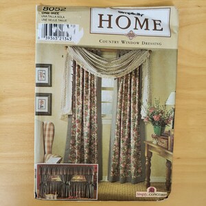 May include: A vintage sewing pattern for country window dressing. The pattern features a floral curtain design with a valance and trim. The package has the word "HOME" and "Simplicity" printed on it. The pattern is labeled "8052" and "ONE SIZE".