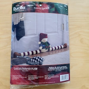 May include: A snowman door draft, 21 x 10.5 inches, made of felt. The snowman has a burgundy hat, a green scarf, and a blue shirt. The body is striped burgundy and white. The product is in a plastic package.