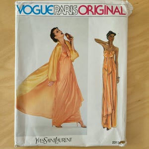 May include: A Vogue Paris Original sewing pattern envelope, number 2313, featuring an Yves Saint Laurent design. The cover displays a photograph and an illustration of a floor-length, strapless, orange gown with a matching long, flowing coat.