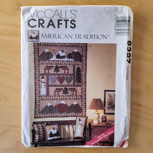 May include: A McCall's Crafts pattern titled "American Tradition" featuring a quilt design with snow-covered mountains, trees, hearts, and a snowman. The pattern also includes designs for matching throw pillows. The pattern is for easy foundation paper piecing.