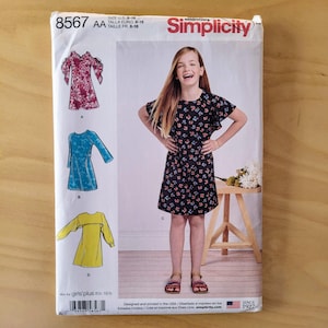 May include: A sewing pattern for girls' dresses, sizes 8-16. The pattern includes three different styles: a dress with ruffled sleeves, a long-sleeved dress, and a dress with a ruffle at the neckline. The pattern is from Simplicity and is designed and printed in the USA.