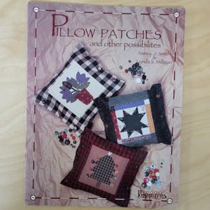 May include: A book cover titled "PILLOW PATCHES and other possibilities" featuring three decorative pillows with patchwork designs. The pillows have floral, star, and Christmas tree motifs. Various colorful buttons are scattered around the pillows.