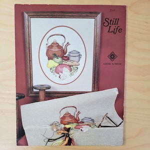 May include: Cross stitch pattern for a still life featuring a teapot, a bowl, bread, fruit, and cheese. The pattern is titled "Still Life" and is from Cross 'n Patch.
