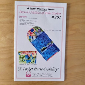 May include: A pattern for a pocket purse, featuring a blue floral design. The pattern includes a diagram of the purse open, measuring 4.25 inches wide by 8.5 inches high, and closed, measuring 4.25 inches wide by 3.25 inches high. The text reads "A Pocket Purse-O-Nality".