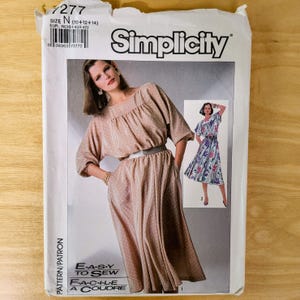 May include: Simplicity sewing pattern featuring a woman in a polka dot dress with a matching belt. The pattern includes the text "E-A-S-Y TO SEW" and "F-A-C-I-L-E A COUDRE". The pattern size is N (10+12+14).