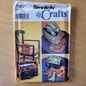 May include: Simplicity Crafts sewing pattern number 7087, one size, for making a sewing machine carrying case, a sewing machine tote bag, and a sewing machine chair caddy. The pattern shows a blue and red plaid tote bag, a blue and green floral chair caddy, and a green and brown floral sewing machine carrying case.