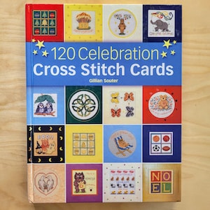 May include: A book titled "120 Celebration Cross Stitch Cards" by Gillian Souter. The cover features a colorful grid of cross stitch patterns for various occasions, including birthdays, holidays, and general celebrations.
