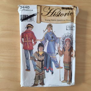 May include: A Simplicity Historic sewing pattern envelope, number 5448, for a Young Native American Dress in size A, sizes 3-8. The front features illustrations of four children wearing various traditional-style outfits, including fringed tunics, pants, and a headdress, with the text 'Historic' and 'Young Native American Dress' printed on the front.