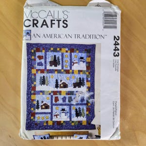 May include: A McCall's Crafts pattern envelope featuring a winter-themed quilt design. The quilt design includes snowmen, trees, houses, and mittens. The text "AN AMERICAN TRADITION" is displayed on the envelope.